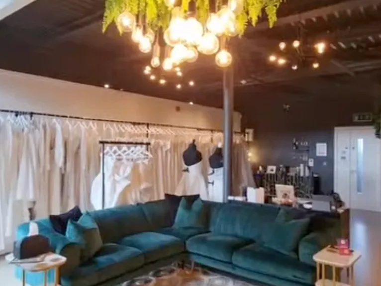 The emerald velvet sofa under the fern and Edison-bulb chandelier, gown rails behind